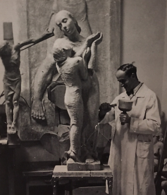 Schwarz-Wei&szlig; Fotografie des K&uuml;nstlers Hermann Amrhein in seinem Atelier. Er bearbeitet gerade mit Hammer und Mei&szlig;el eine Frauenskulptur. Im Hintergrund sind andere fertige Werke zu sehen